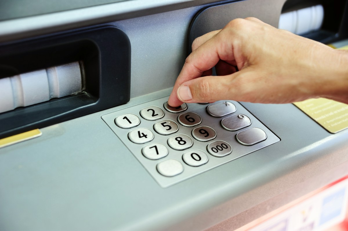 A hand entering a PIN code on an ATM keypad