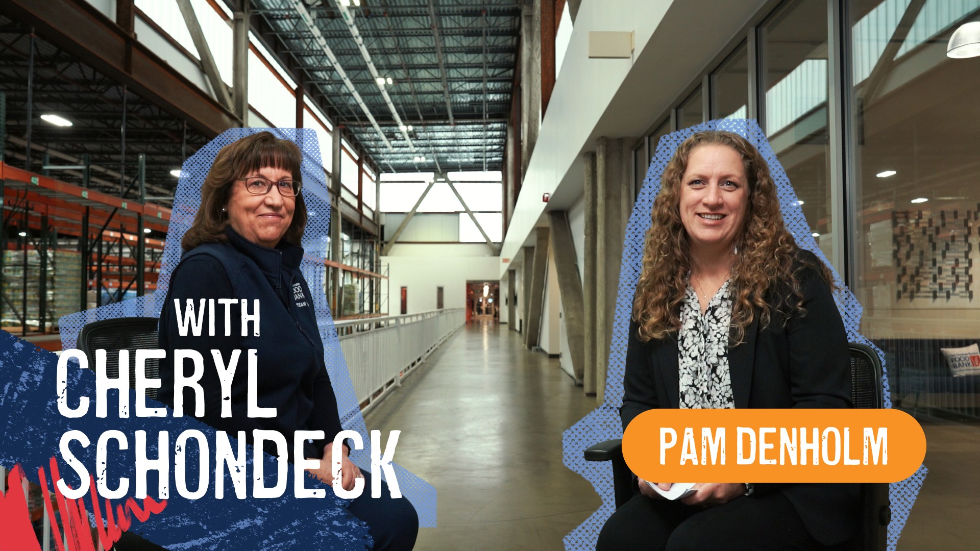Two women sit facing the camera on office chairs in a wide hallway with warehouse shelving on the left and glass-walled rooms on the right.