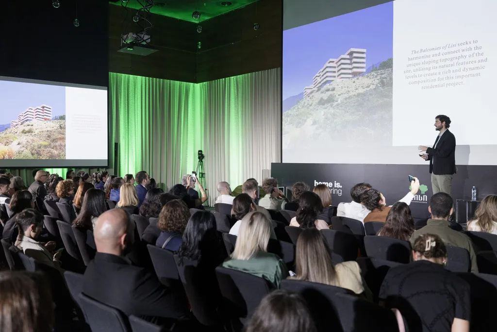 Architecture presentation with audience in a dark room, large screen displaying visuals.