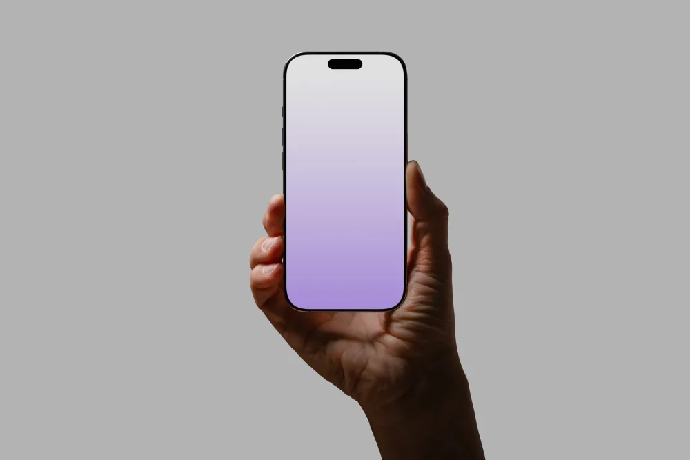 Hand holding an iPhone with a gradient purple screen against a gray background. Minimalist composition with natural light highlighting the hand and sleek phone design.