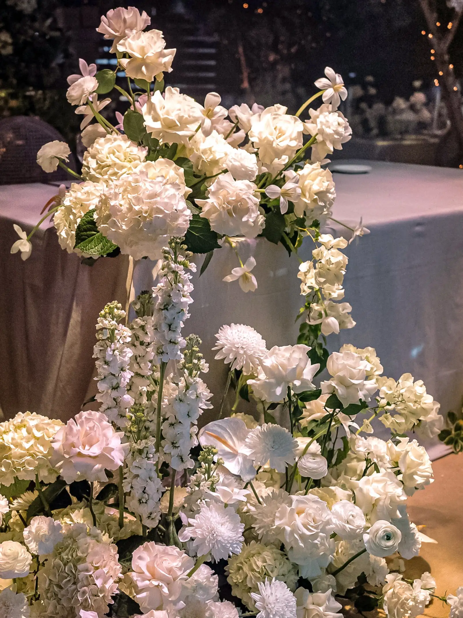 Arreglo floral en tonos blancos con rosas, hortensias y flores de tallo alto en un ambiente elegante.