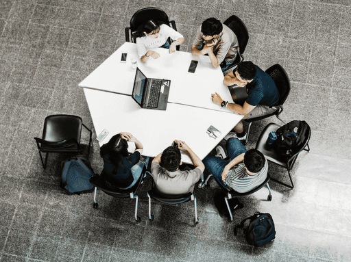 Students working together around a table with a laptop in between them.