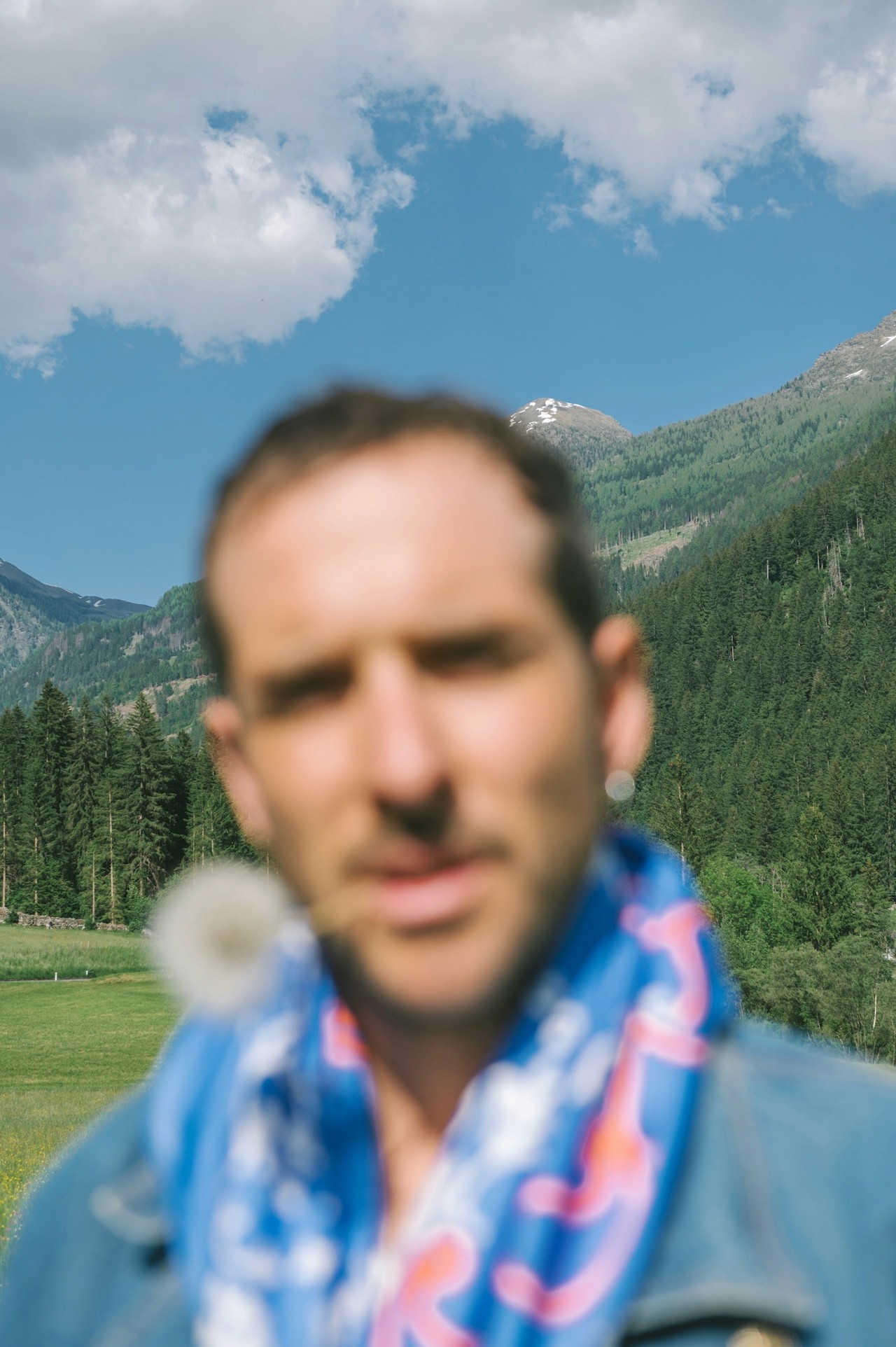 A man standing outdoors with mountains in the background, softly out of focus.