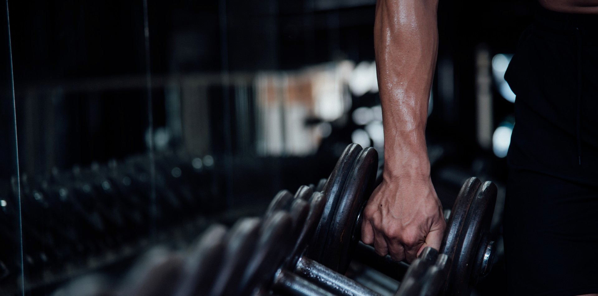 Homem dentro de academia, pegando pesos para iniciar atividades físicas.