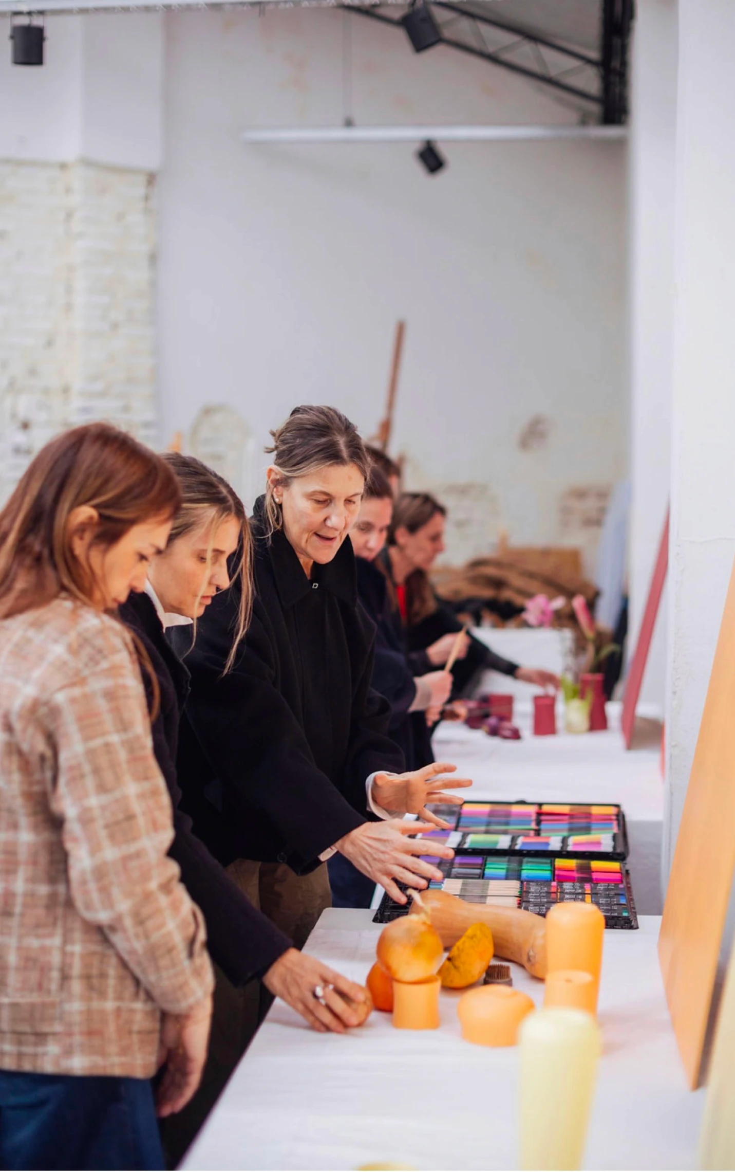 Varias mujeres participan de un taller creativo alrededor de una mesa, explorando materiales, muestras de color y composiciones en tonos cálidos.