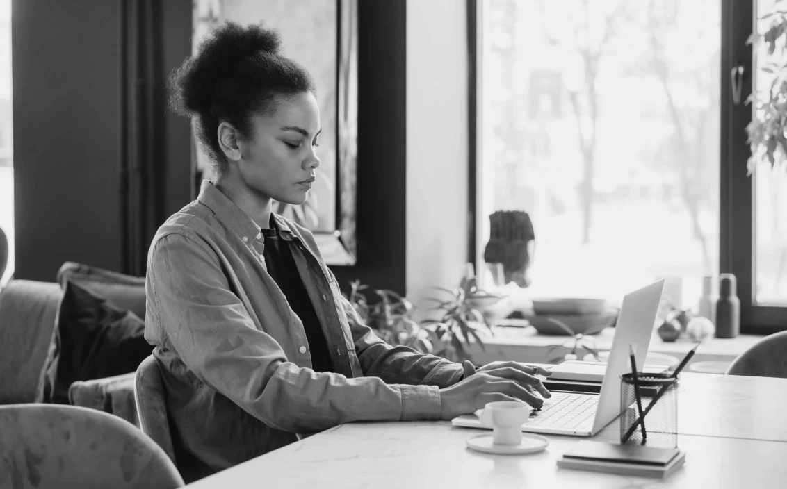 A woman typing on a computer working on her product design portfolio at a cafe