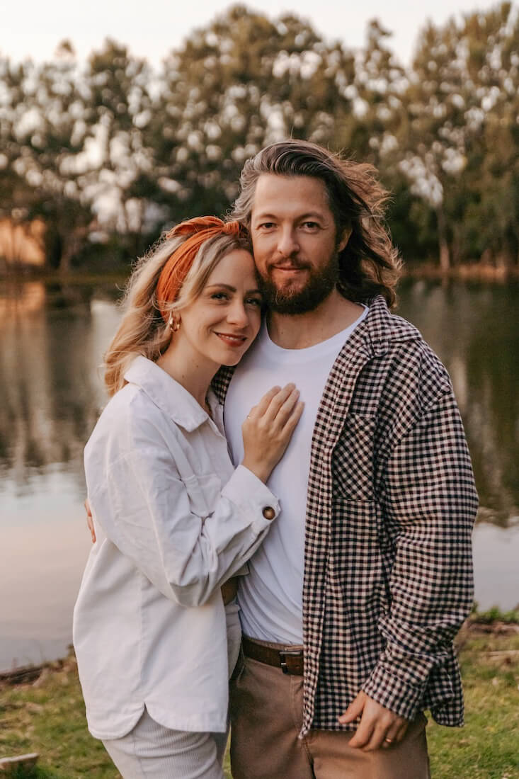 Silvino and Amy standing together by a pond during family photoshoot, Amy snuggled into his chest