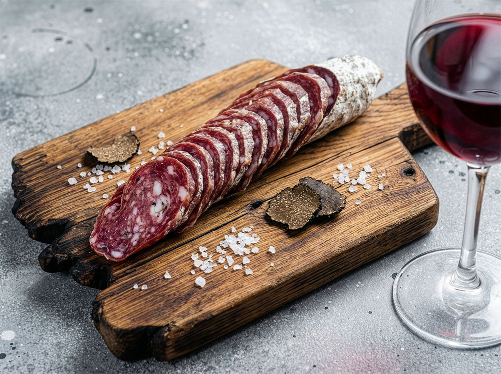 Sliced black truffle salami on a wooden board with truffles and a glass of red wine from Porcellino Artisanal Meats in Lakewood, CO.