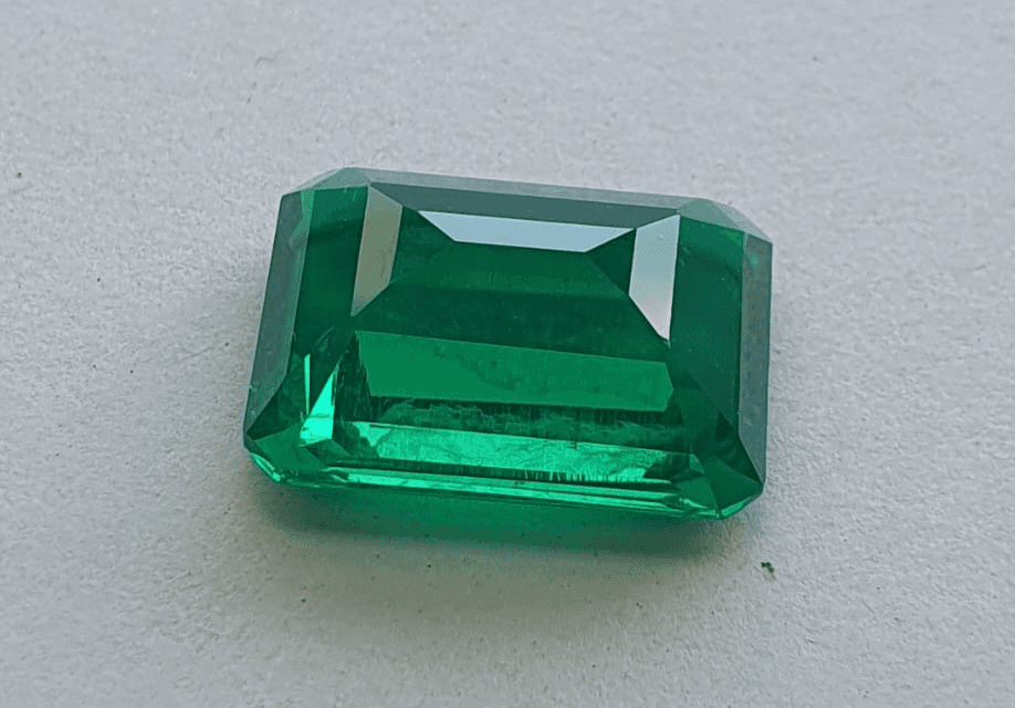 A loose lab grown emerald gemstone resting upside down on its flat table facet, exposing its pointed pavilion and angular pavilion facets.