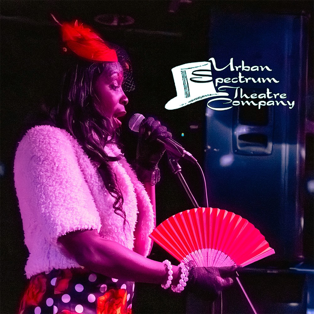 A female musician singing passionately into a microphone on stage during a live theater performance.