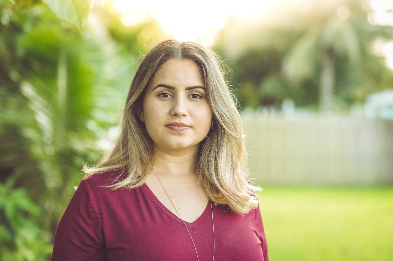 photo of a yound woman in a red top standing in a field and looking at the camera