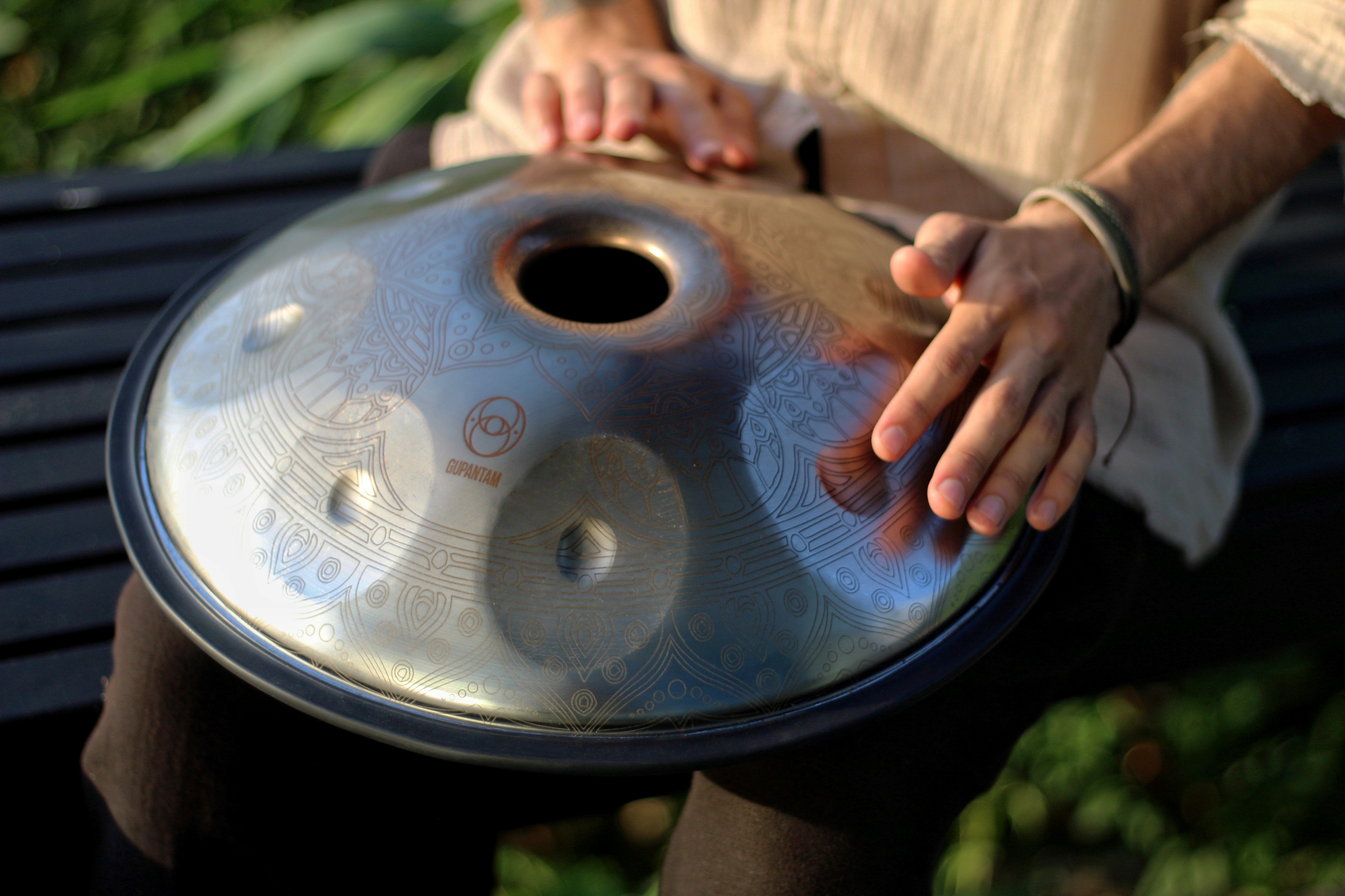 Someone is sitting and touching the mini handpan on their lap with both hands.