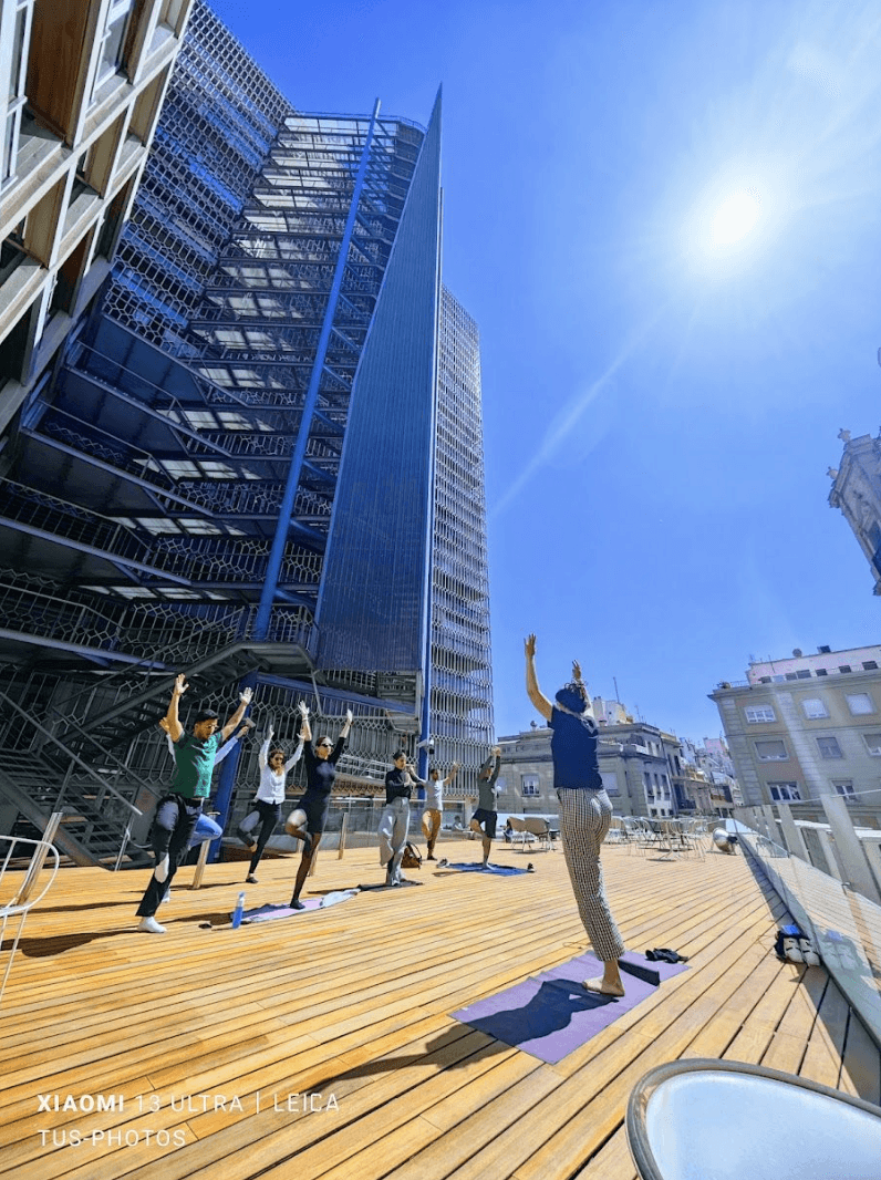 A sunny day in an urban area with people walking on a wooden boardwalk and modern buildings in the background.