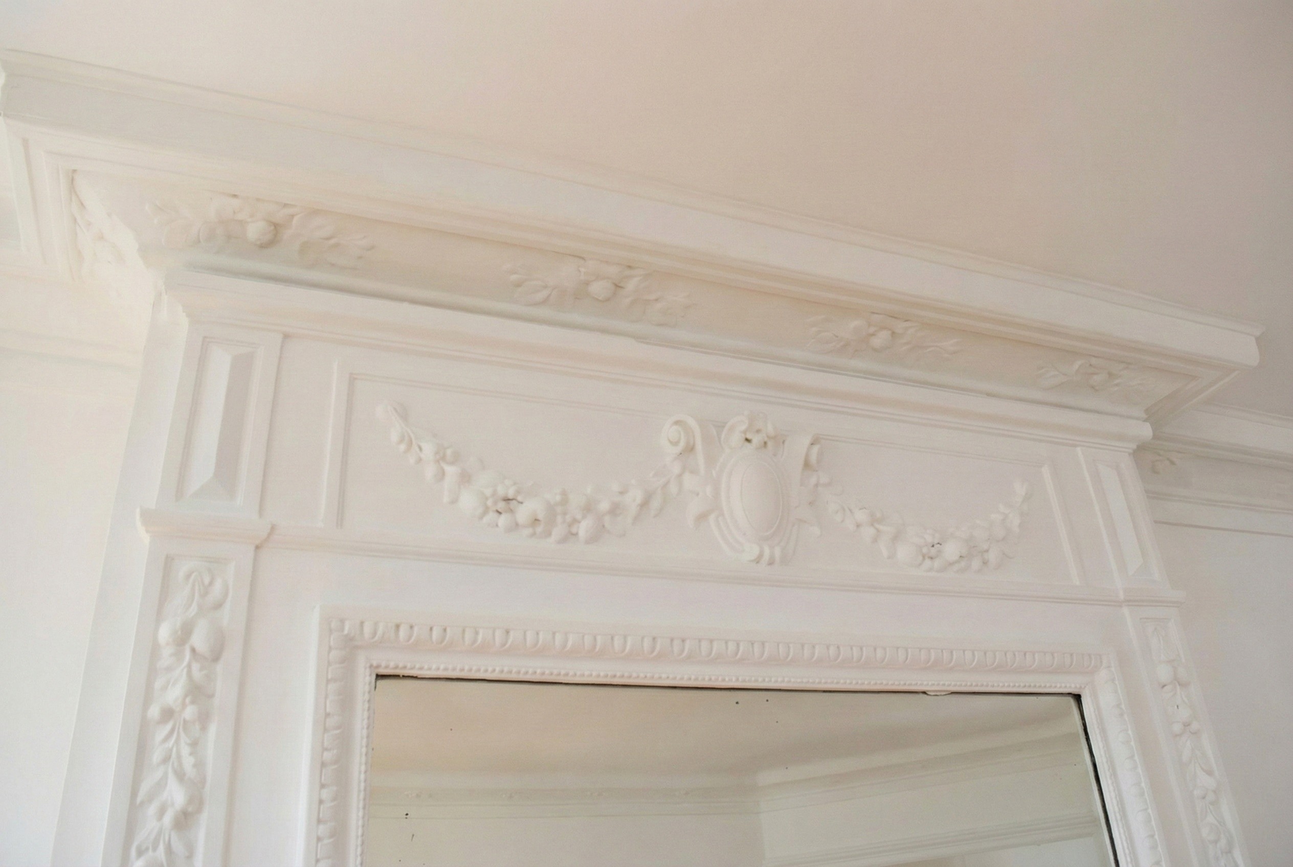 Zoom sur les ornements d'une cheminée ancienne en bois sculpté blanc, emblématique du standing parisien.