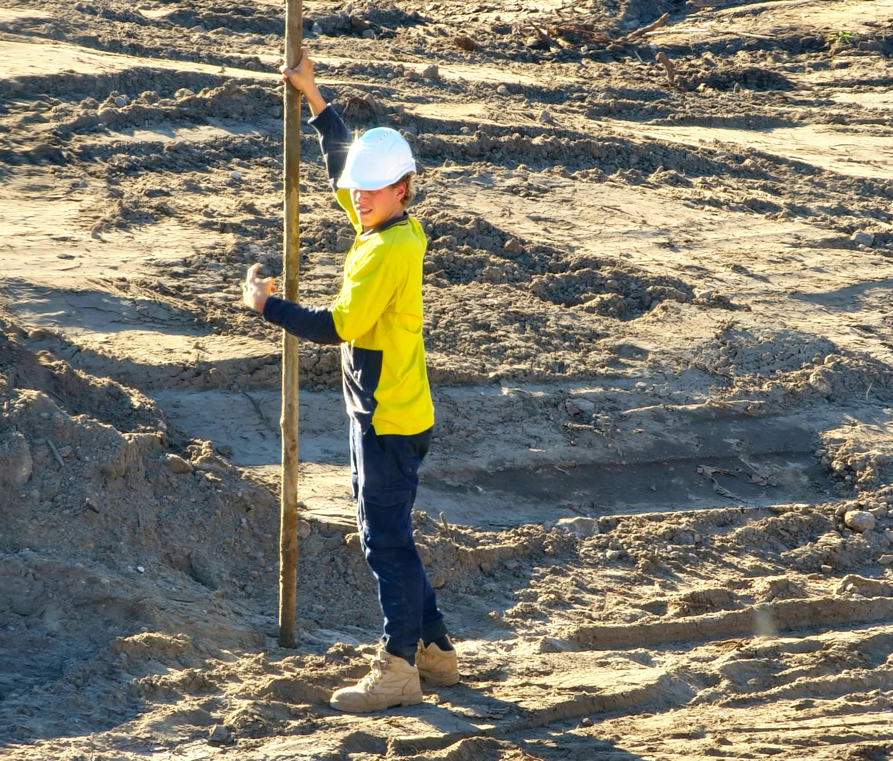 a little boy standing next to a pole in the sand