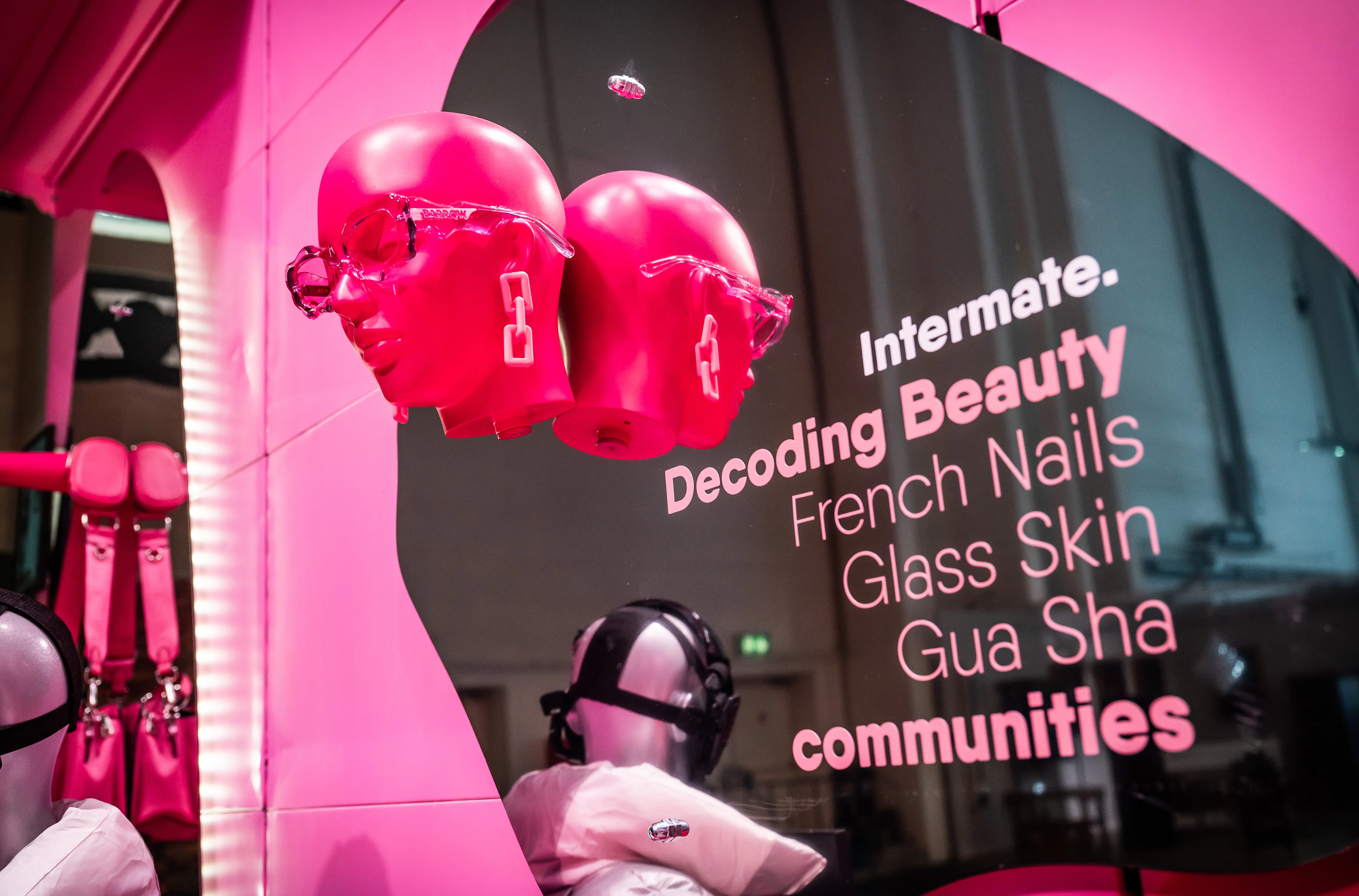 Pink sculpted heads with sunglasses beside the lettering Decoding Beauty communities in the Intermate display window.
