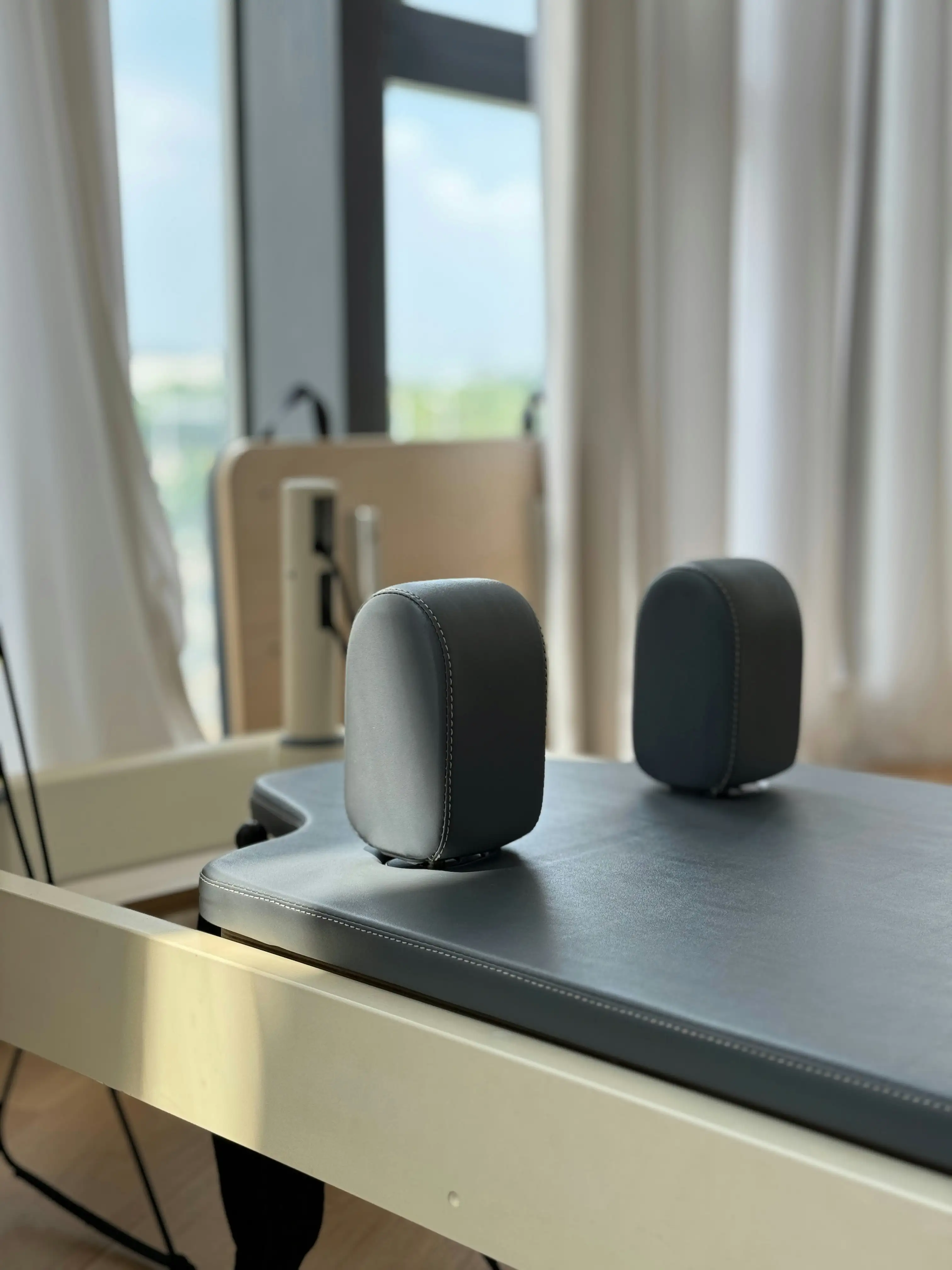 Nahaufnahme schwarzer Leder-Kopfstütze am Pilates Reformer mit unscharfem Holz-Geräteständer im Hintergrund eines Wellness-Studios