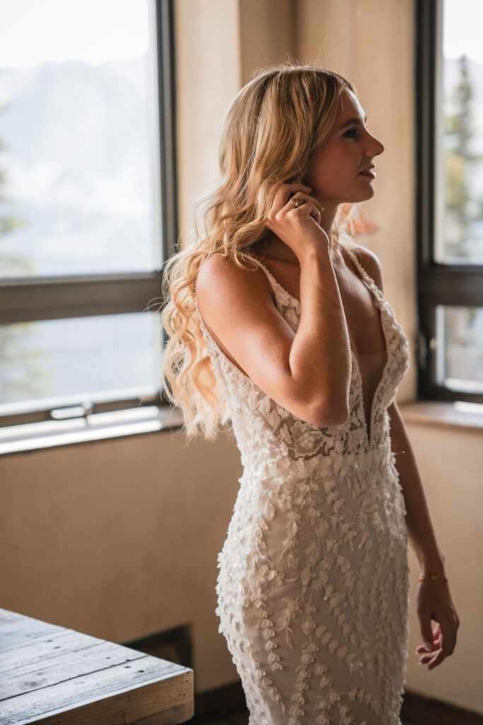 Bride adjusting hair by window light at Smith Cabin Aspen wedding getting ready suite
