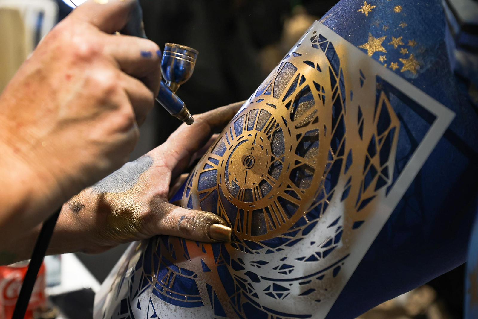 Black-and-white photograph of a person in motion, creating a blurred effect, standing in a field of tall grass and wildflowers under a cloudy sky, capturing a sense of freedom and nature."