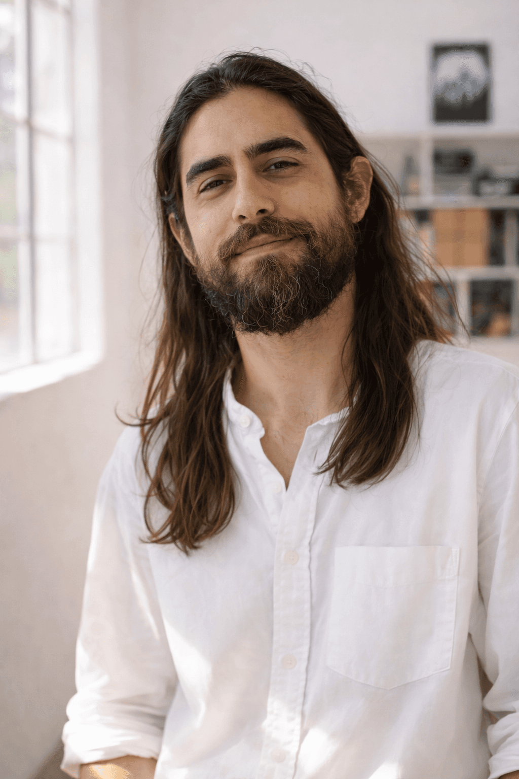 In an office setting, a man with long hair and a beard sits at a desk, engaged in his tasks.