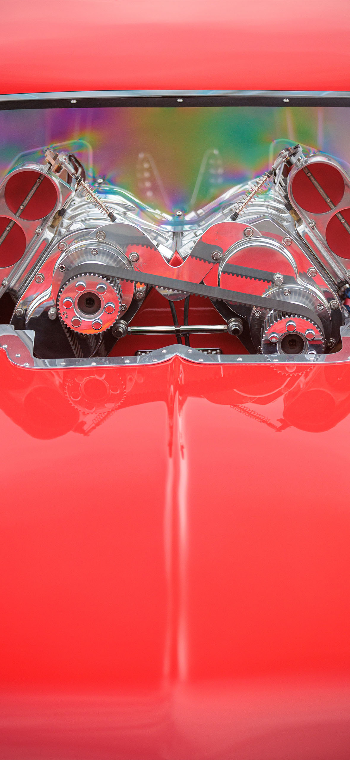 Close-up of a red car's engine, showing polished metal parts and a serpentine belt.