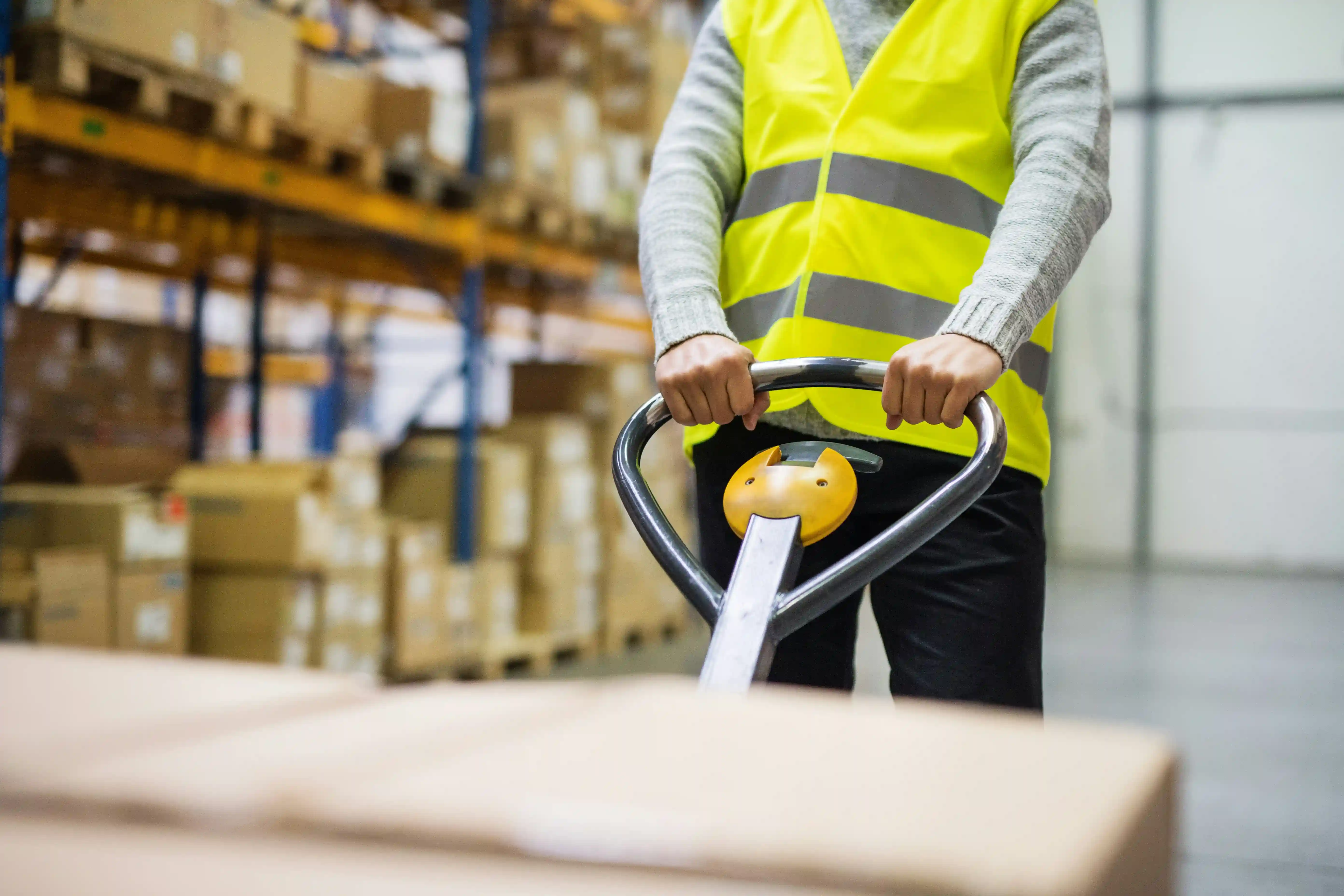 close-up of a warehouse worker wearing a green high-vis jacket pulling a pallet trolley along
