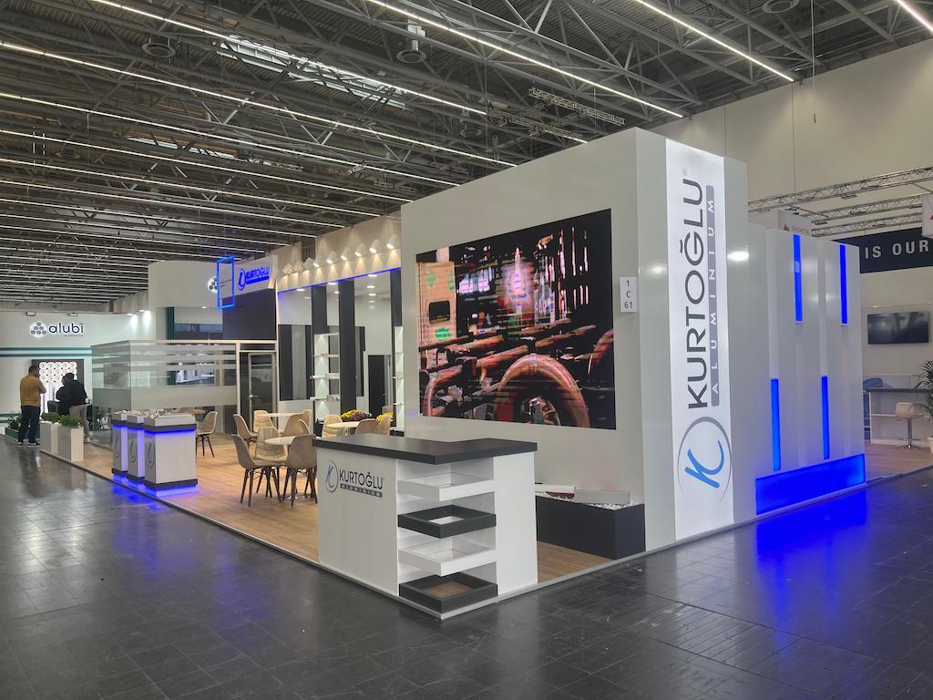 Exterior view of the Kurtoğlu exhibition stand at Aluminium Düsseldorf, featuring an illuminated brand wall, product display niches, and meeting areas.
