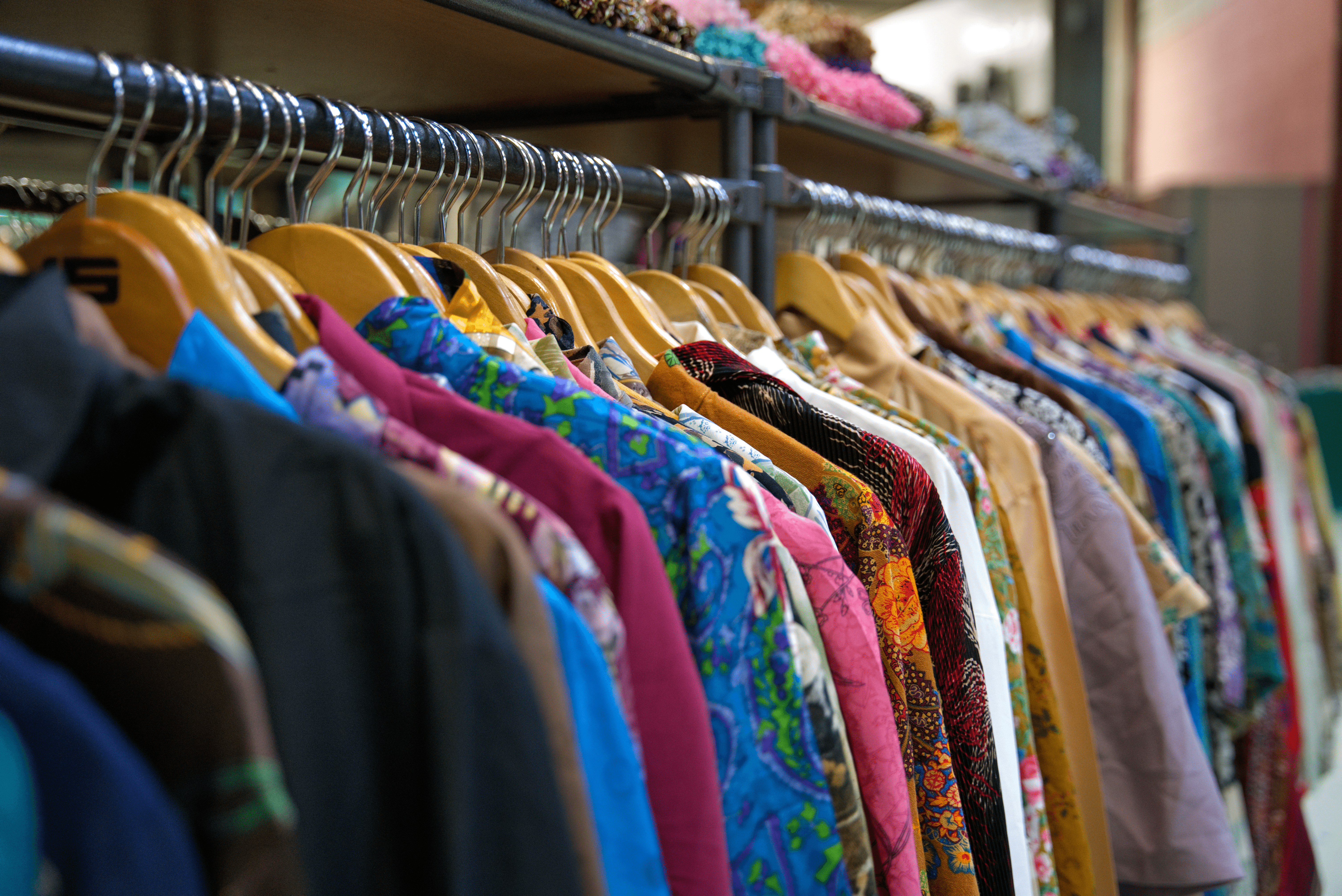 Rack of colorful vintage shirts on wooden hangers in clothing store.