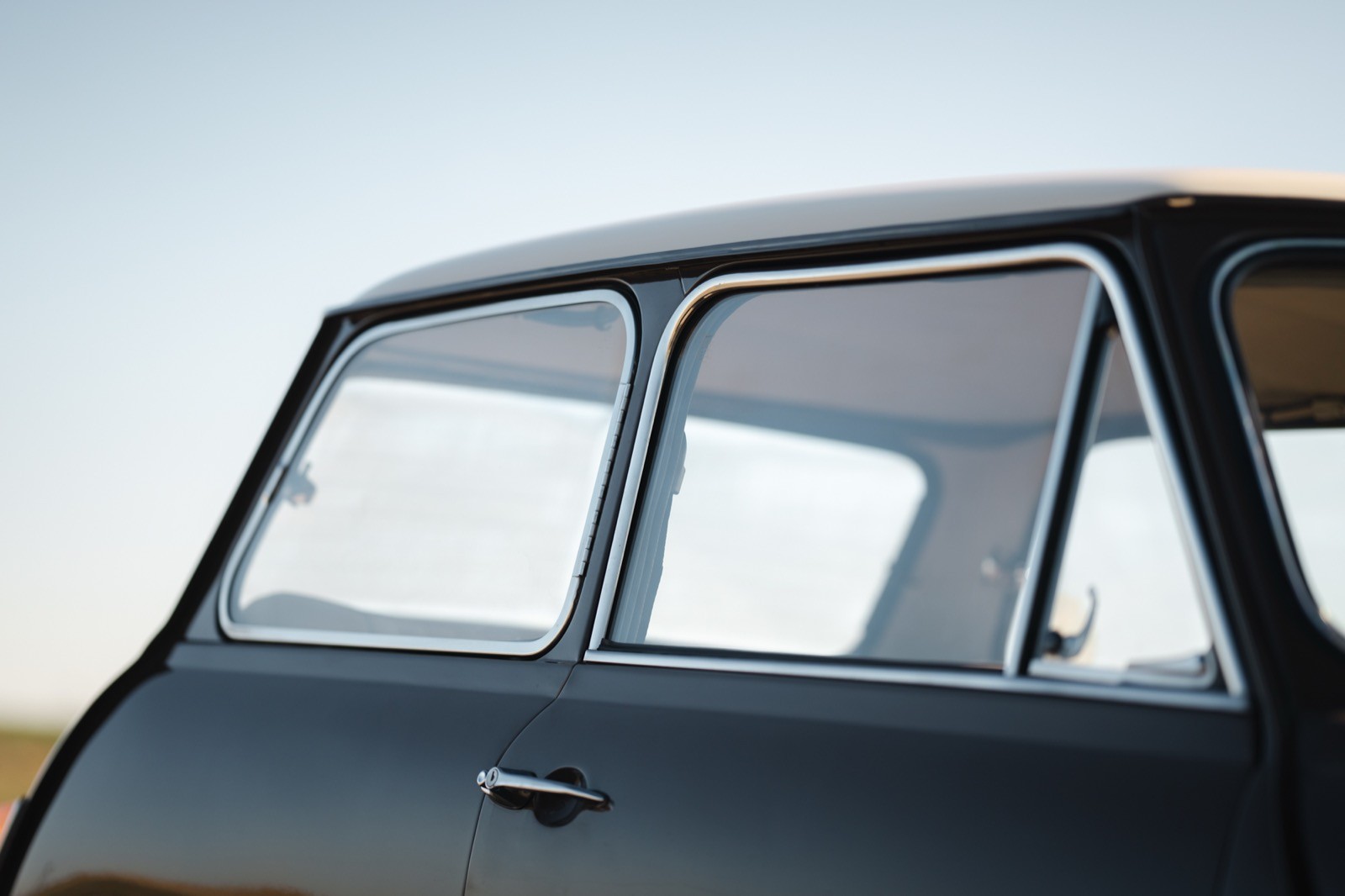 Close-up of the rear window and roofline of a vintage car against a clear blue sky.