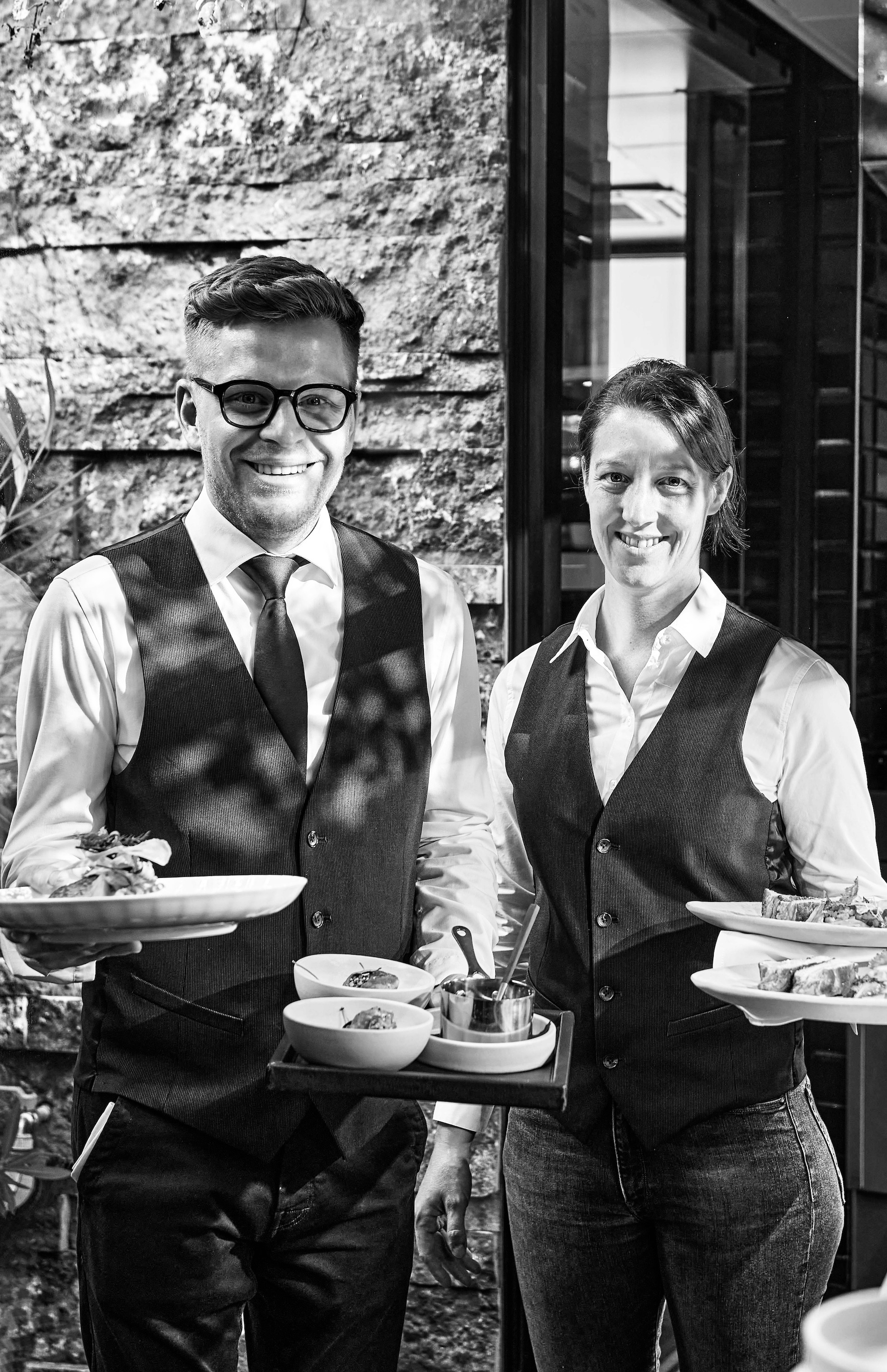 Smiling service team members presenting freshly prepared dishes at La Fontanella