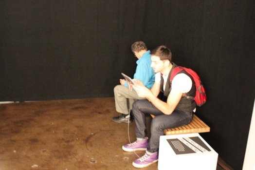 two men sitting on a bench with mobile devices in their hands