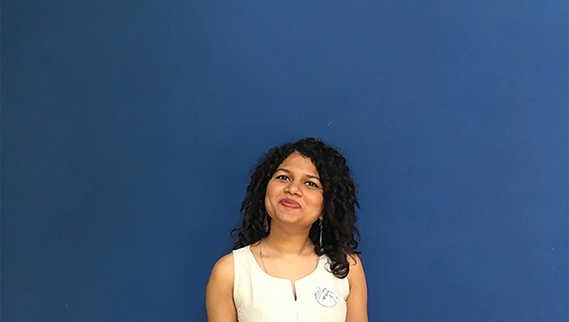 A photo of a woman wearing a white dress and standing in front of a blue screen.