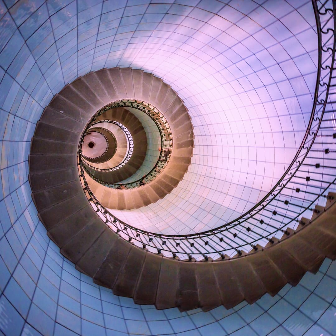 A photo of a spiral staircase in a lighthouse from below, representing many steps leading to higher ground