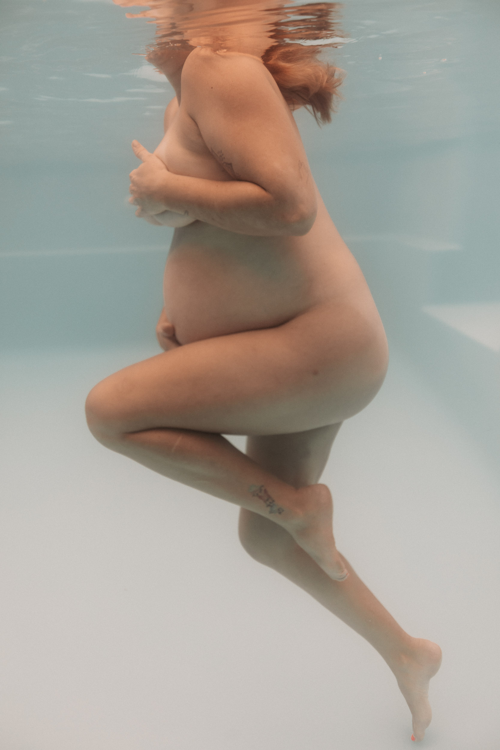 Underwater maternity portrait in Mackay featuring pregnant mother floating in soft blue pool light