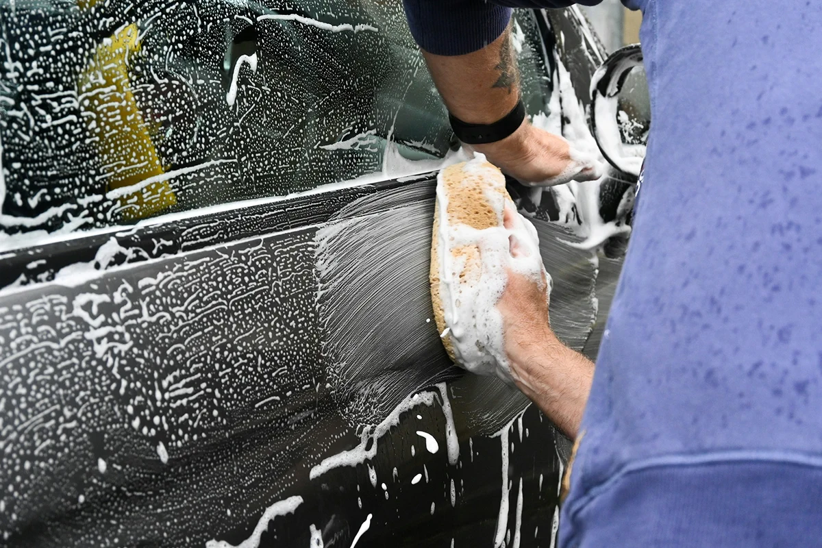Detailing technician hand washing a vehicle surface with soap foam during exterior car cleaning.