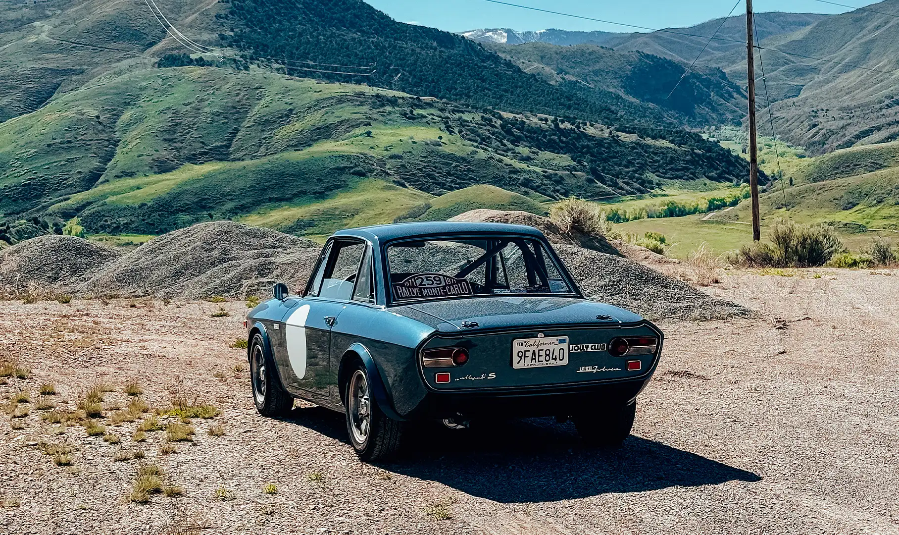 A blue Lancia Fulvia sports car parked in the mountains