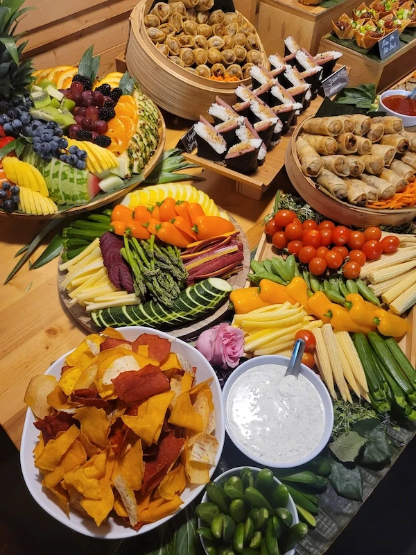 Abundant Asian-Hawaiian catering table with fruits, musubi, and spring rolls