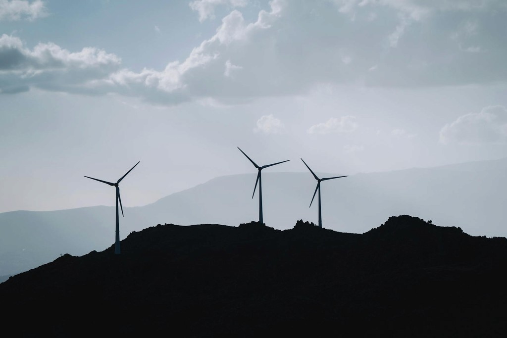Silhouetted wind turbines on a hill against a cloudy sky, representing renewable energy and sustainability.