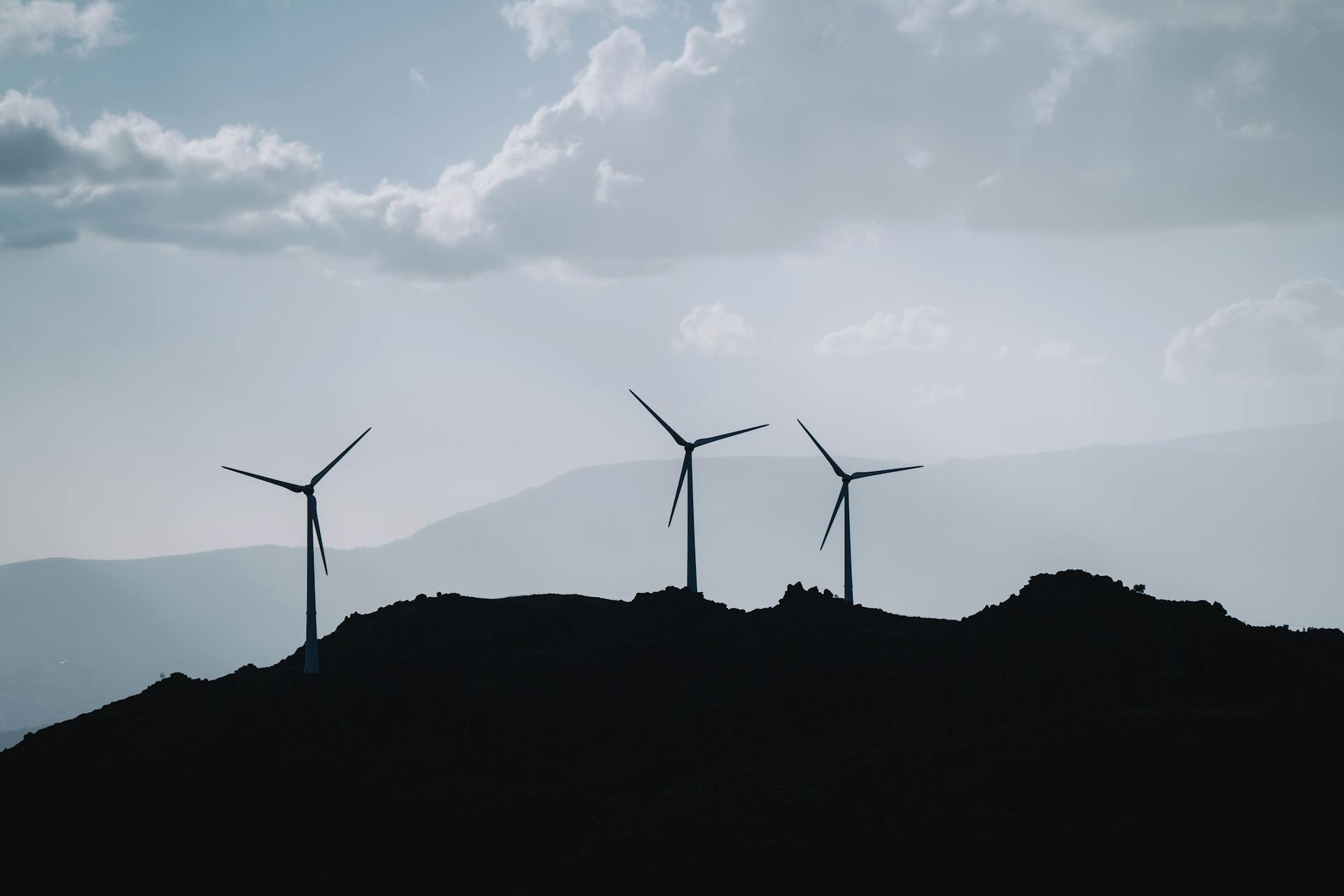 Silhouetted wind turbines on a hill against a cloudy sky, representing renewable energy and sustainability.