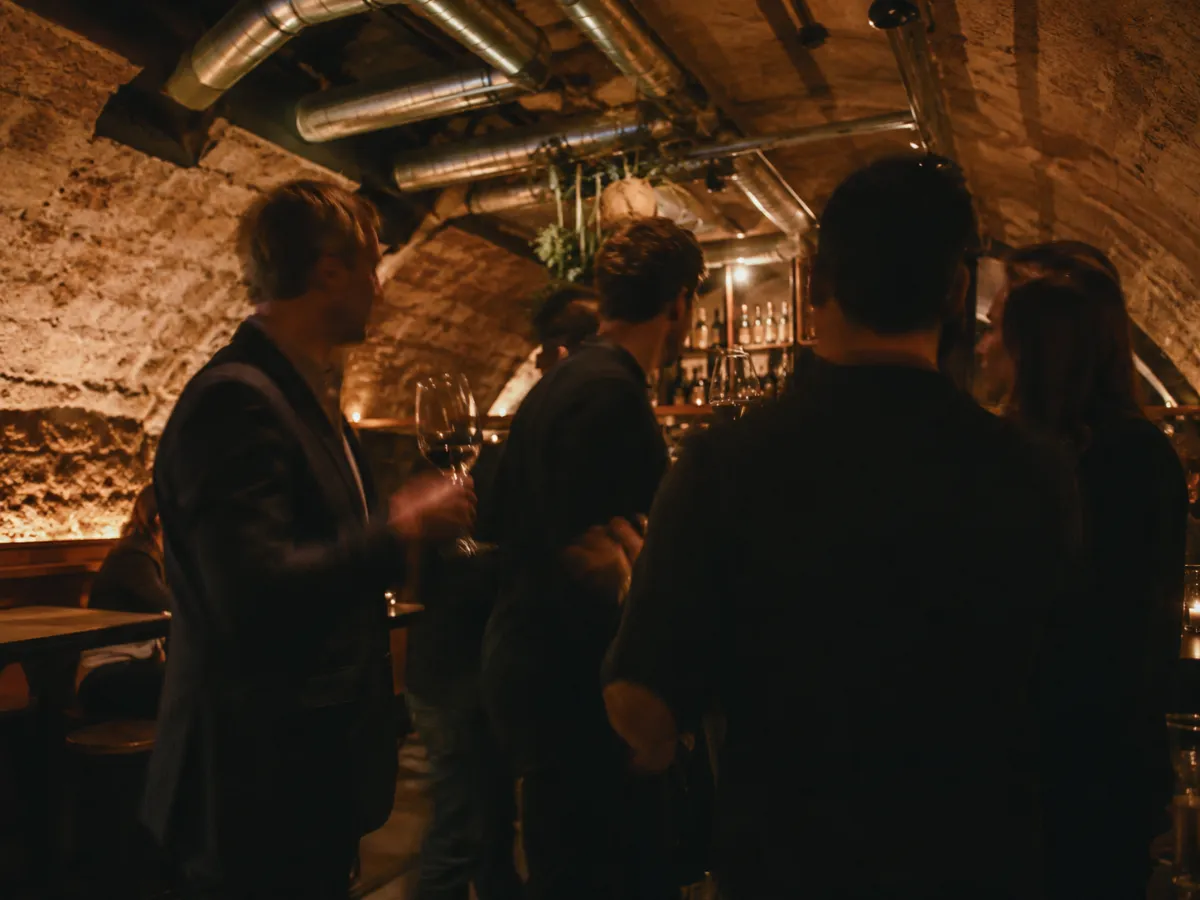 Gäste stehen mit Weingläsern an der Bar im Gewölbekeller