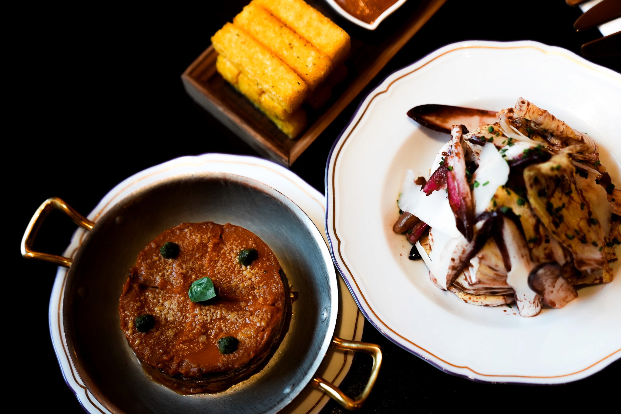 Bride sitting on ground against wall, groom standing nearby