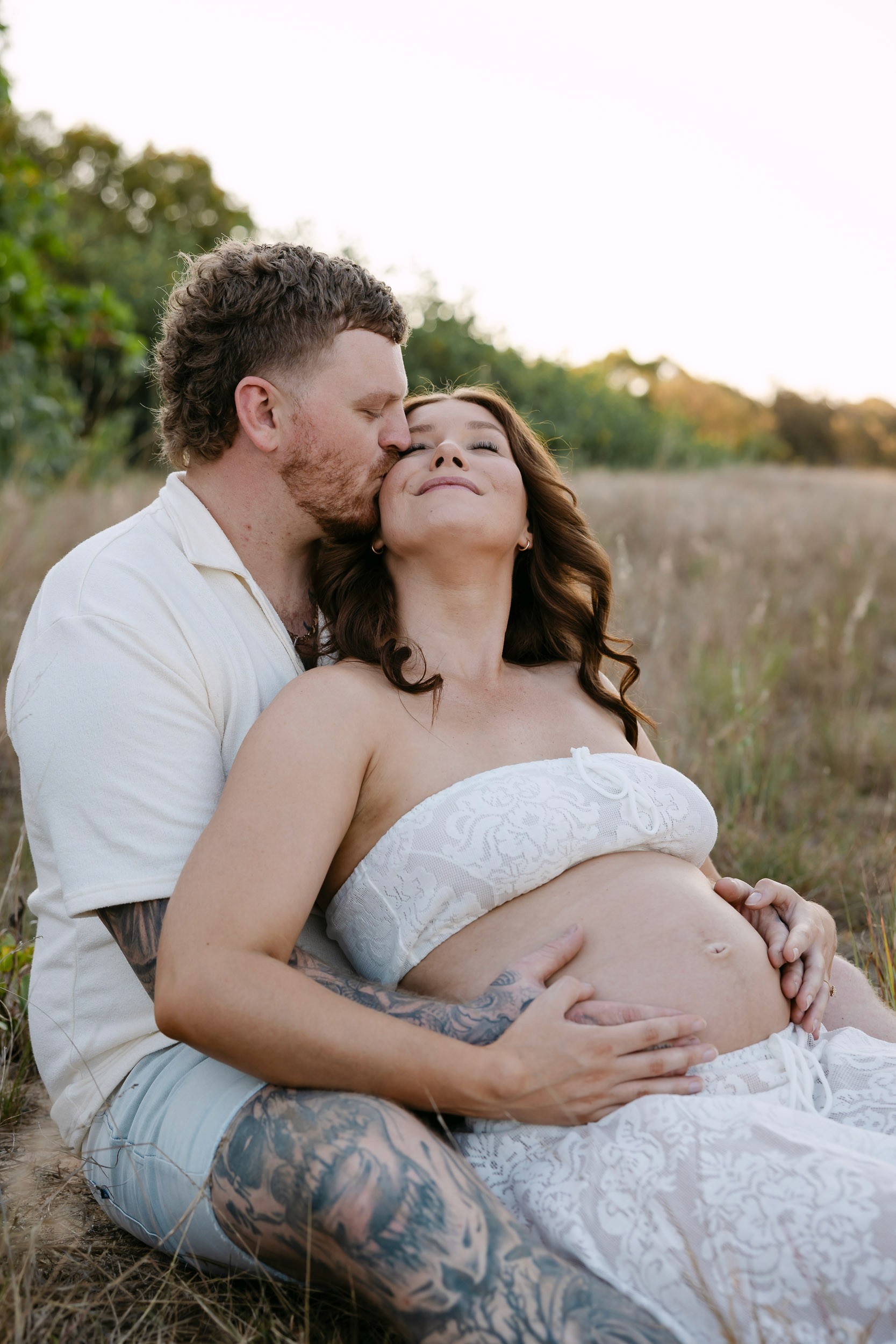 Pregnant couple cuddling in tall grass during maternity photo session Mackay