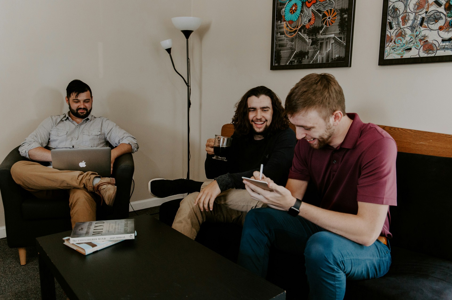 Three people sitting on a couch in a room looking at mobile devices