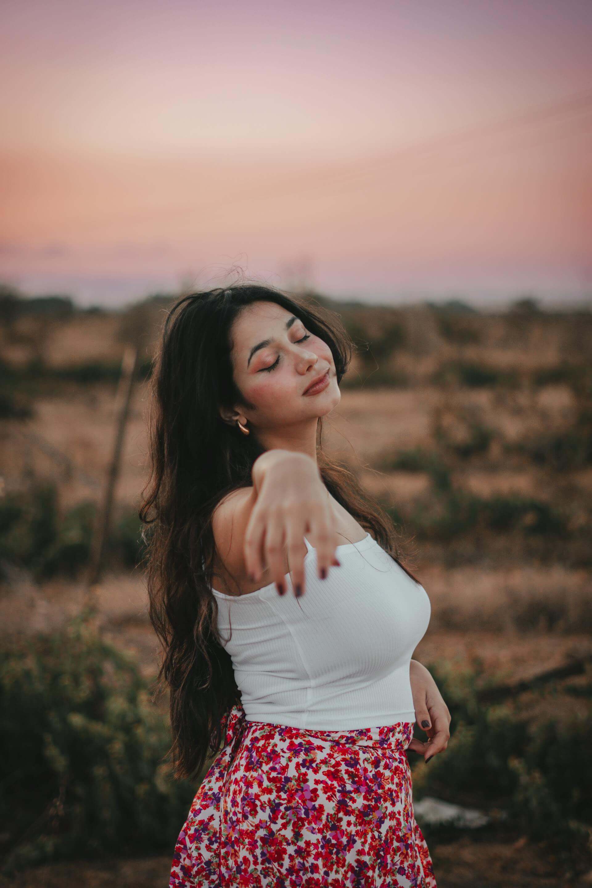 A woman in a floral skirt is gesturing towards the sky with a joyful expression