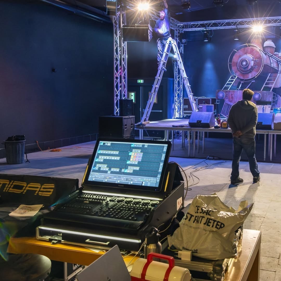 Crew set up lighting and a stage, with a laptop on a flight case in front.