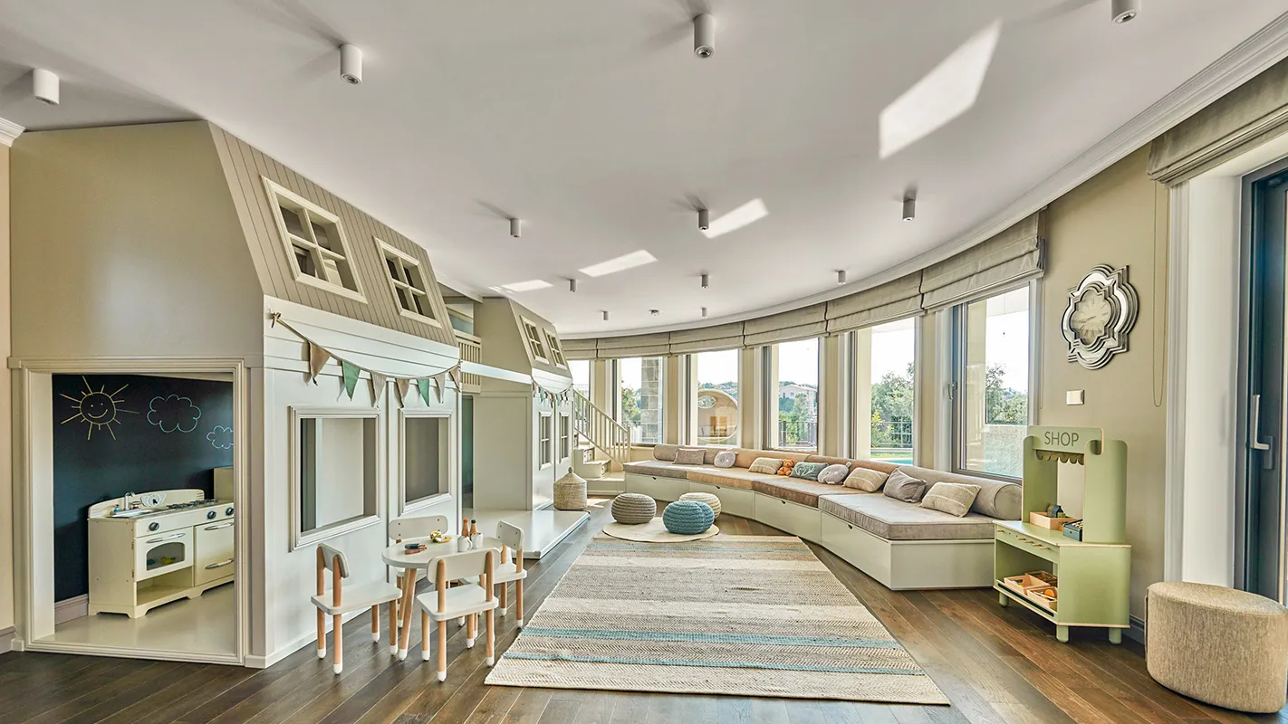 Villa Belmare children’s playroom with built-in playhouse, curved banquette seating, and bright window wall
