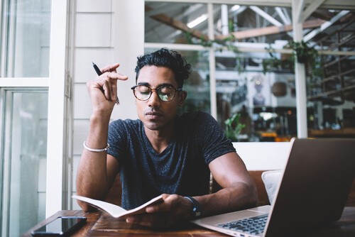 Man reading notebook in front of laptop