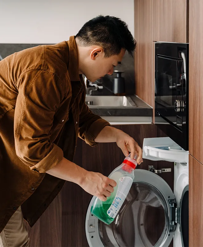 A man pouring laundry detergent into a washing machine in a modern fitted kitchen