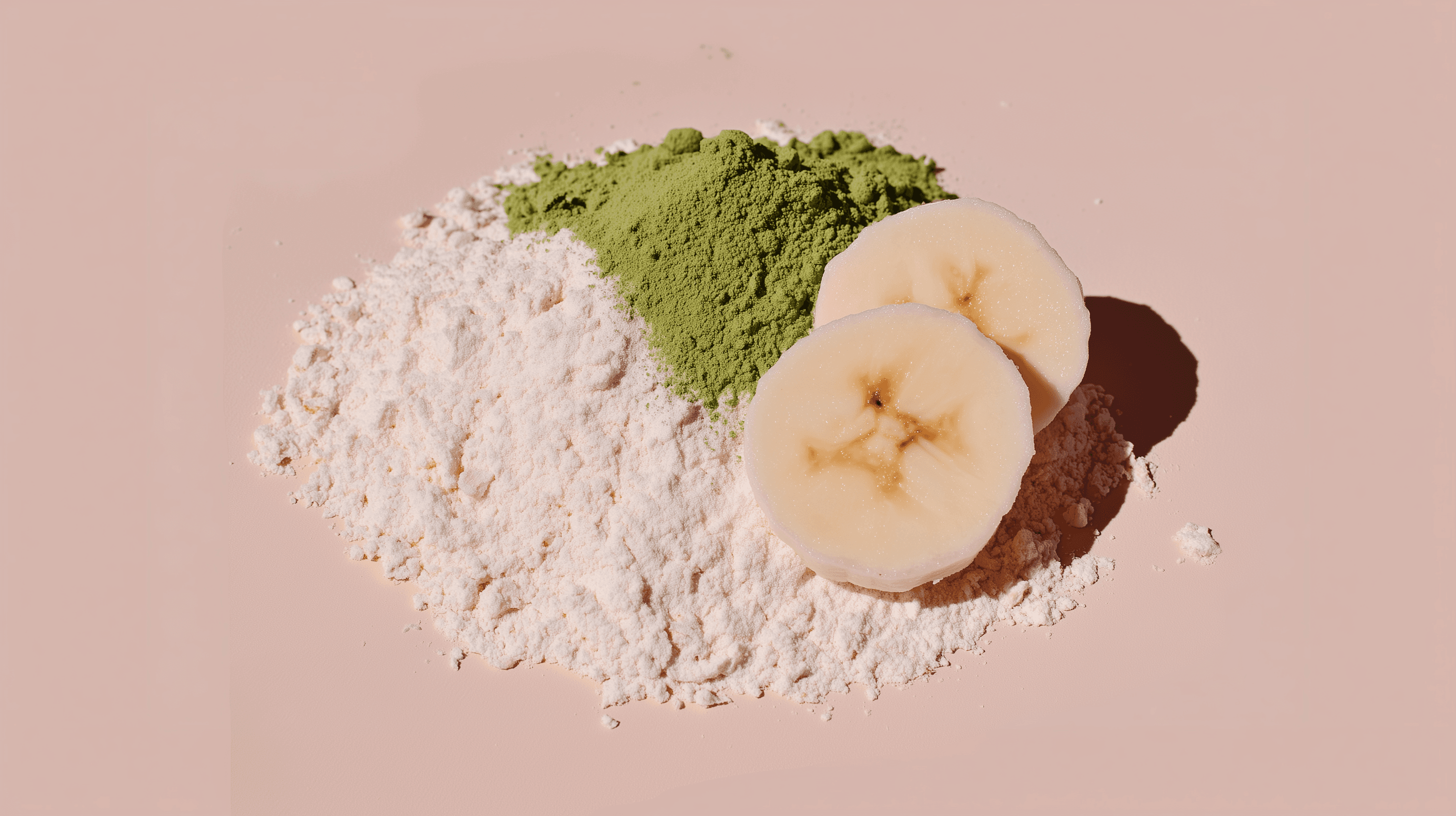 Matcha powder and white protein powder with fresh banana slices on a blush pink background