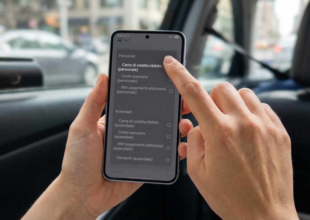 Una mano tiene uno smartphone, sulla schermata è aperta l’app Fluida sulla scelta del metodo di pagamento della nota spese, sta selezionando “con carta di credito”